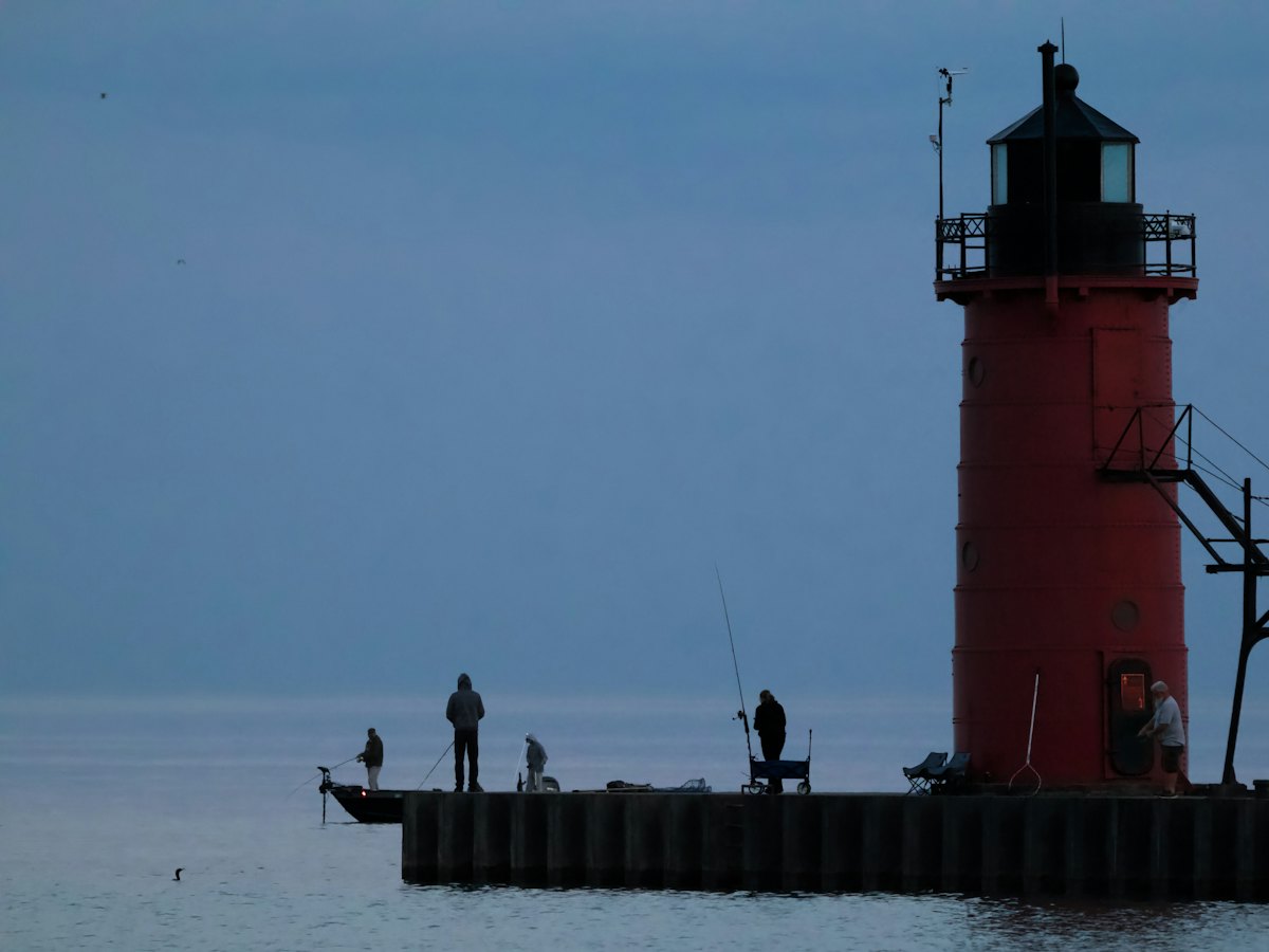 A red lighthouse at the end of a pier at dusk